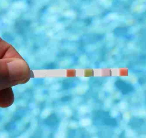 Maão segura fita de como medir o ph da água e piscina ao fundo