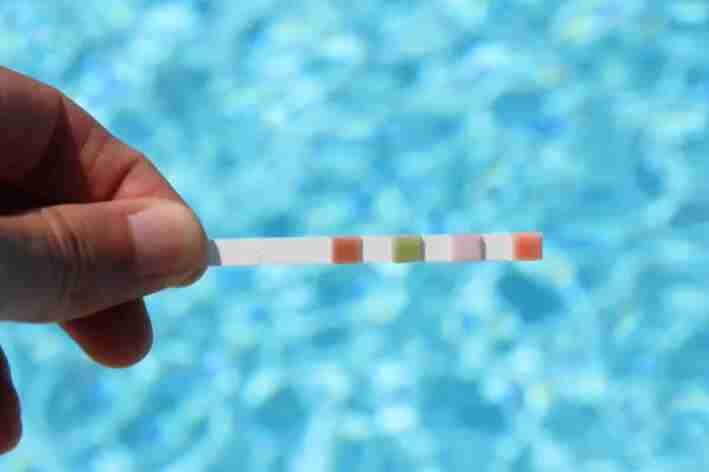 Maão segura fita de como medir o ph da água e piscina ao fundo