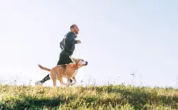 Homem correndo ao ar livre com seu cachorro em um campo aberto, manhã ensolarada, prática de atividade física ao ar livre, vida saudável, bem-estar