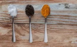 três tipos de temperos diferentes em colheres em cima de uma mesa de madeira